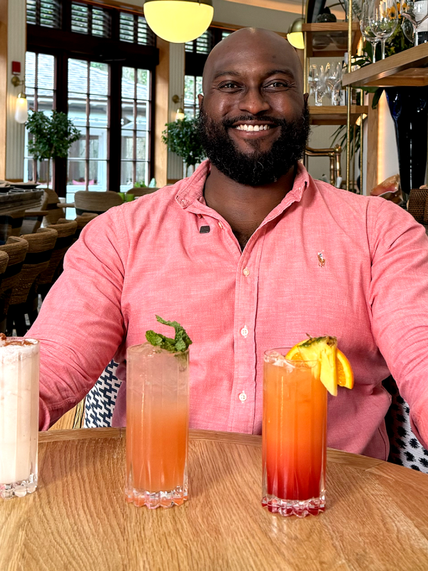 A man in a collared shirt sits with three drinks in front of him.