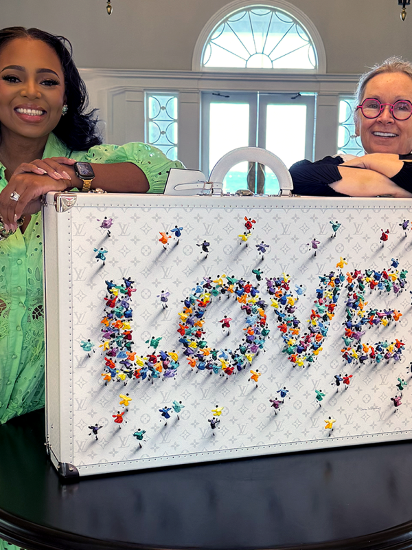 Two women stand in front of a piece of art that says Love.