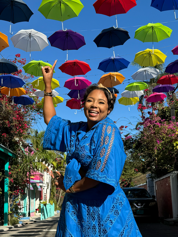 A woman stands on a street with umbrellas hanging in the air.