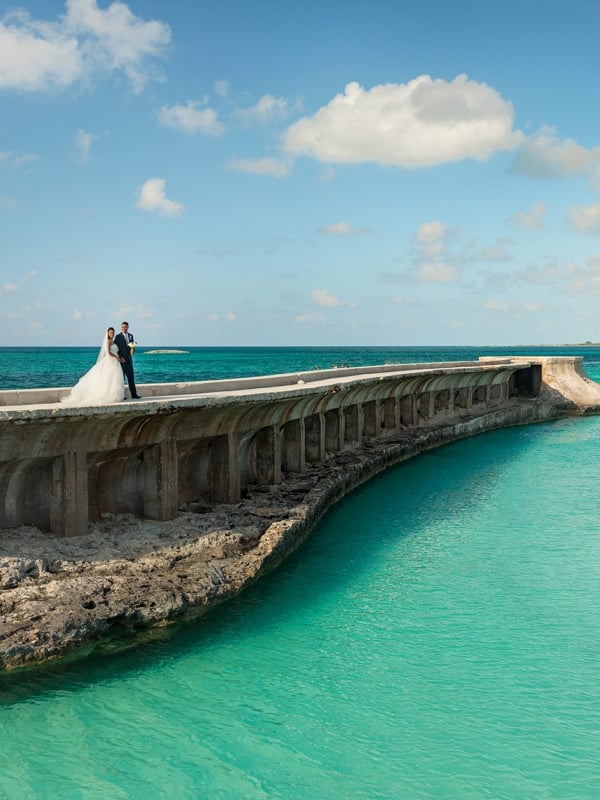 A bride and groom stand on a boardwalk that runs alongside a small river