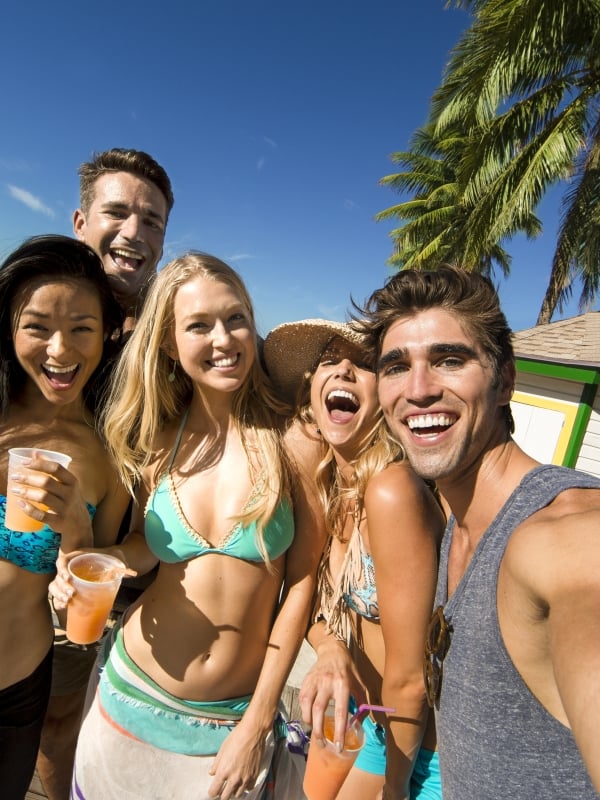 A group of young men and women in bathing suits take a selfie on the beach