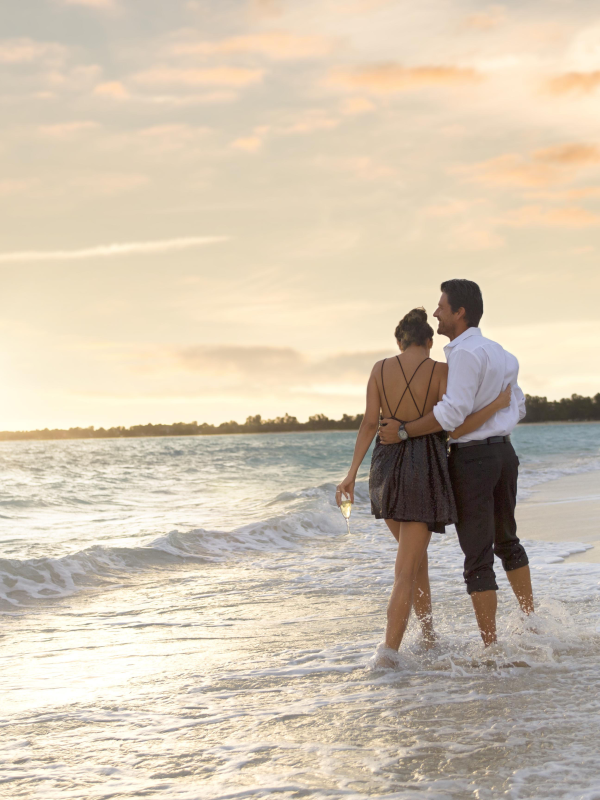 A couple walks along the water's edge on a Bahamas beach at sunset. 