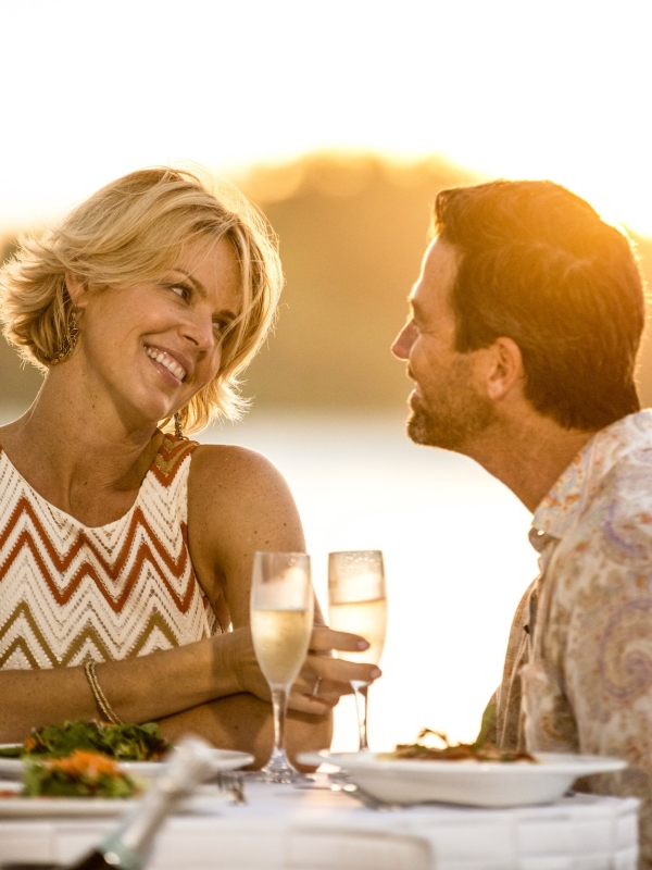 A couple toasts at a patio table at sunset. 