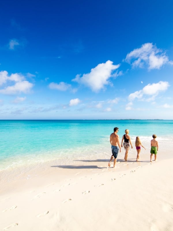 A family of four walks together along a Bahamas beach. 