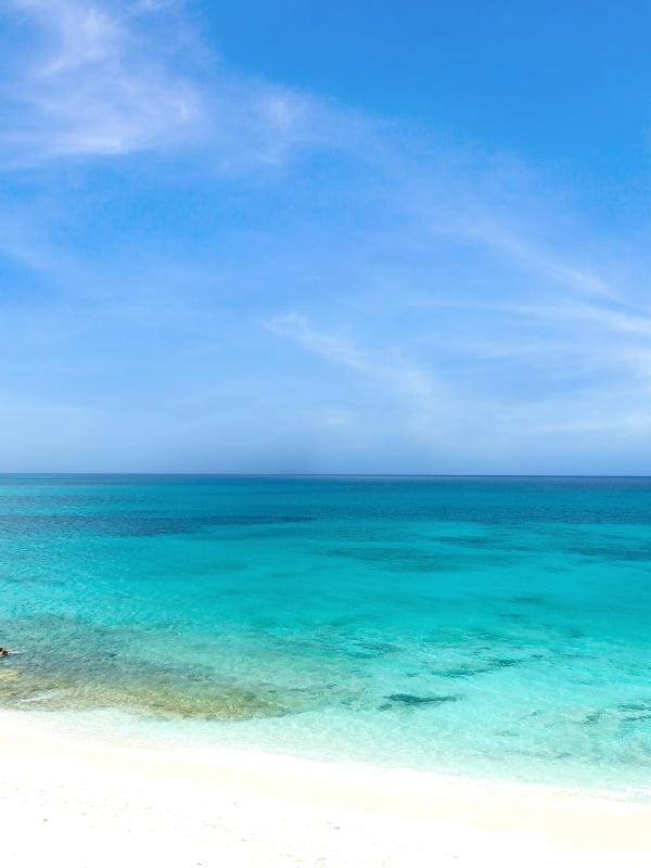 Bright blue sky, clear turquoise waters, and a small boat anchored off the shore of a Bahamas beach. 