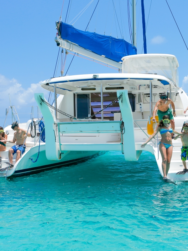 A couple and family prepare to jump off the back of a catamaran into turquoise Bahamas waters.