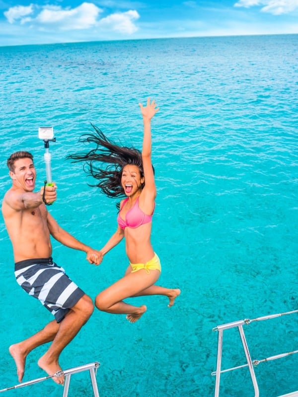 A couple jumps into the water while holding a selfie stick.