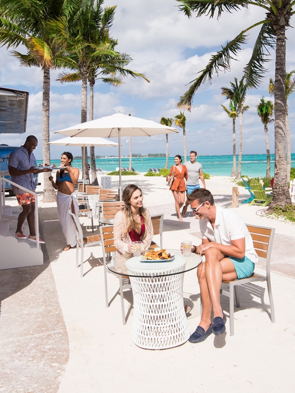 A server exits a pink beachside airstream to serve food to diners.