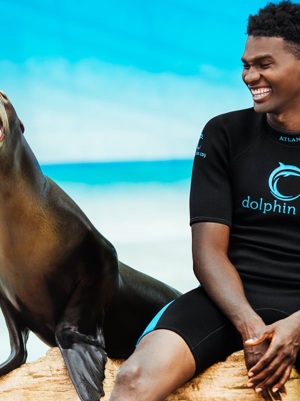 A man sits on a rock next to a playful sea lion.