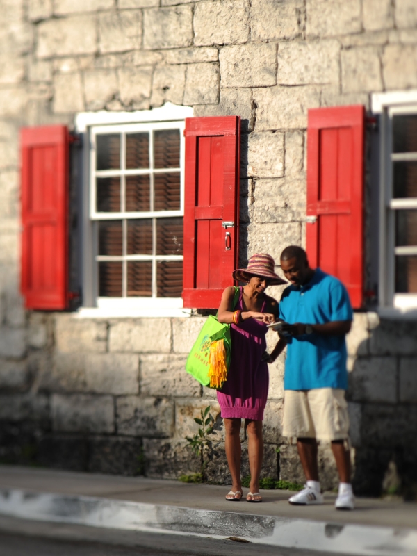 A couple look at a map outside a historic Bahamas building with red shutters.
