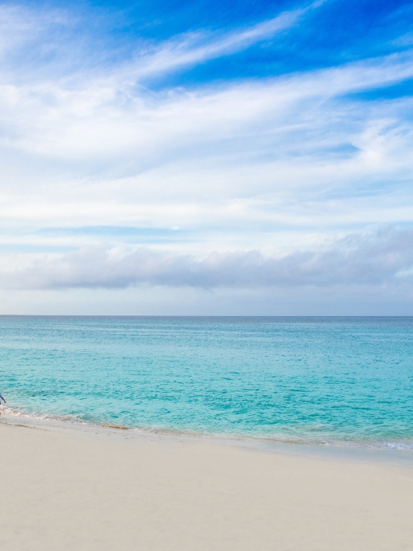 A family of four walks hand-in-hand along a Bahamas beach.