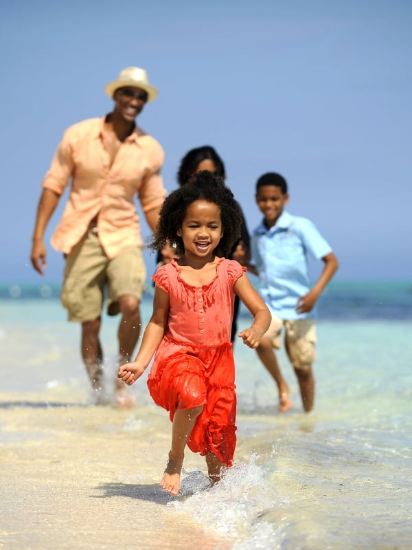 Little girl running in the water with family running behind her