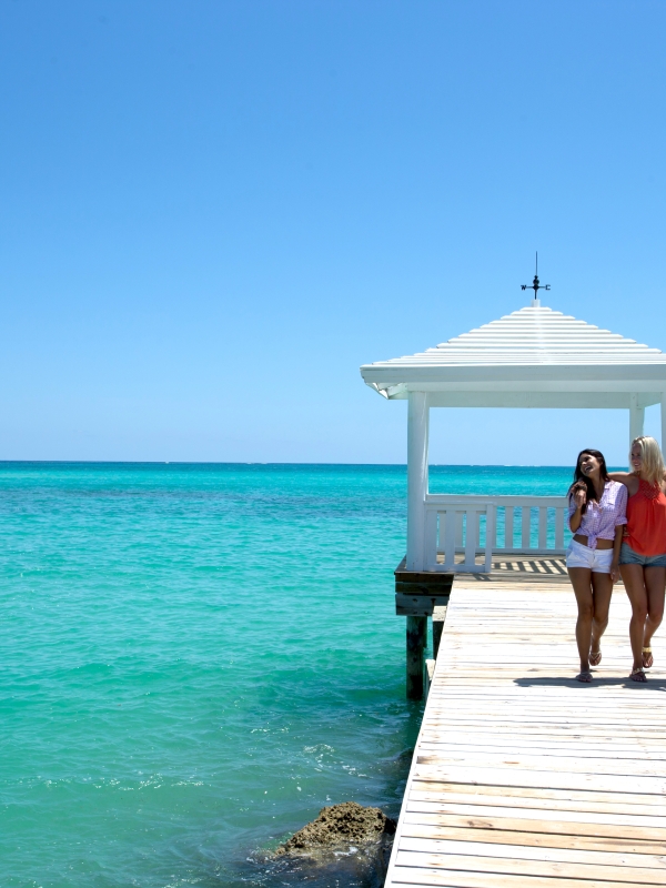 Three women walk arm-in-arm along a boardwalk in The Bahamas.