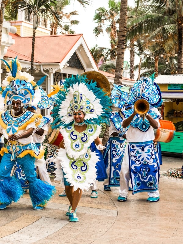 A Junkanoo band in colorful blue costumes plays instruments and dances outdoors in Nassau. 