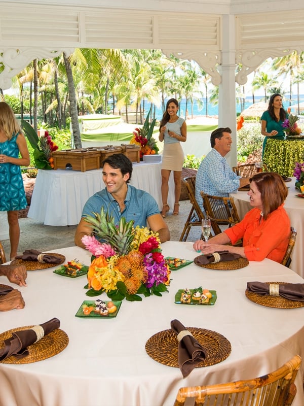 An outdoor restaurant filled with guests covered by a white wooden gazebo.