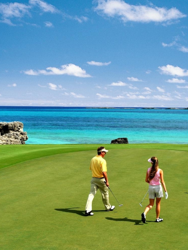 A man and a woman walk towards a hole on a golf course in The Bahamas.