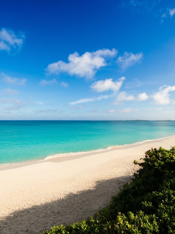 An empty tropical beach with white sand and bright turquoise water.