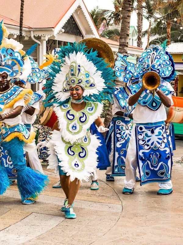 People dressed in intricate costumes walk down a sunny street.