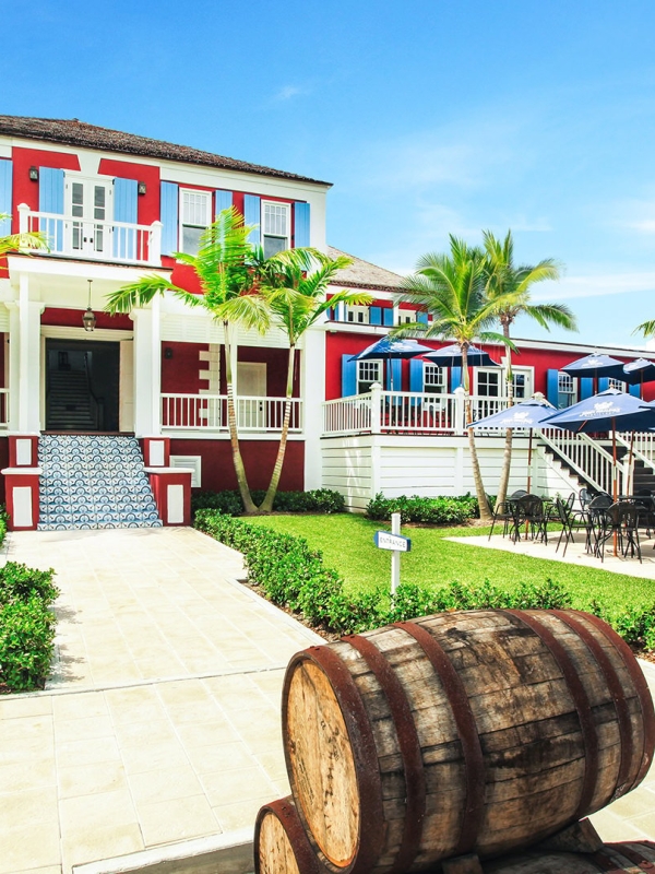 A wooden barrel sits outside of a large red house with patio tables and chairs outside.