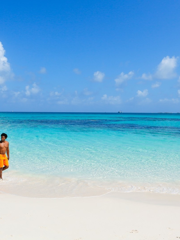 A man and woman walk hand-in-hand down a white sand beach.