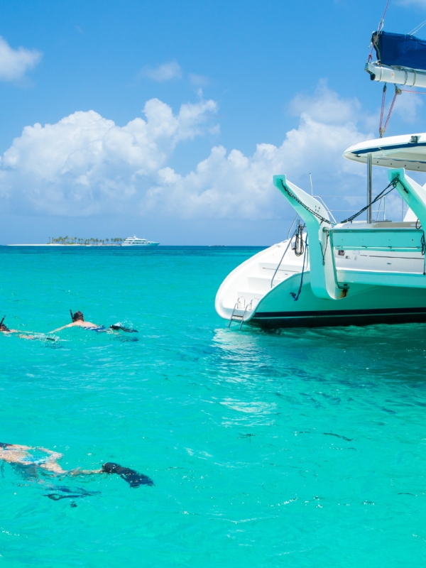 A group of people snorkelling around a catamaran.