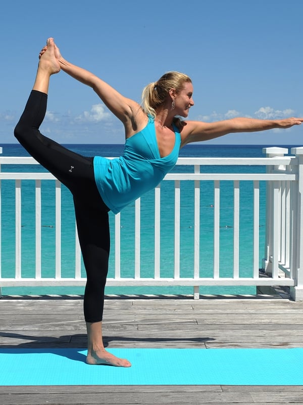 A woman practices yoga on a deck overlooking the ocean.