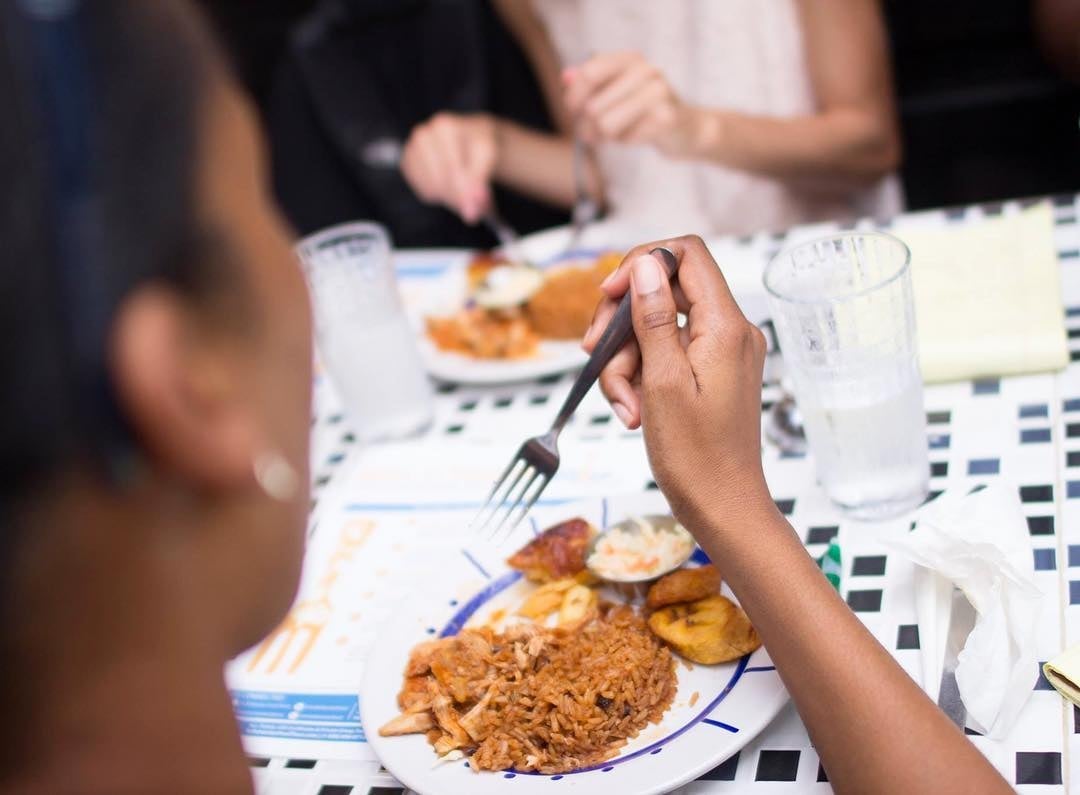 A woman lifts a fork to sample a plate of Bahamian food. 