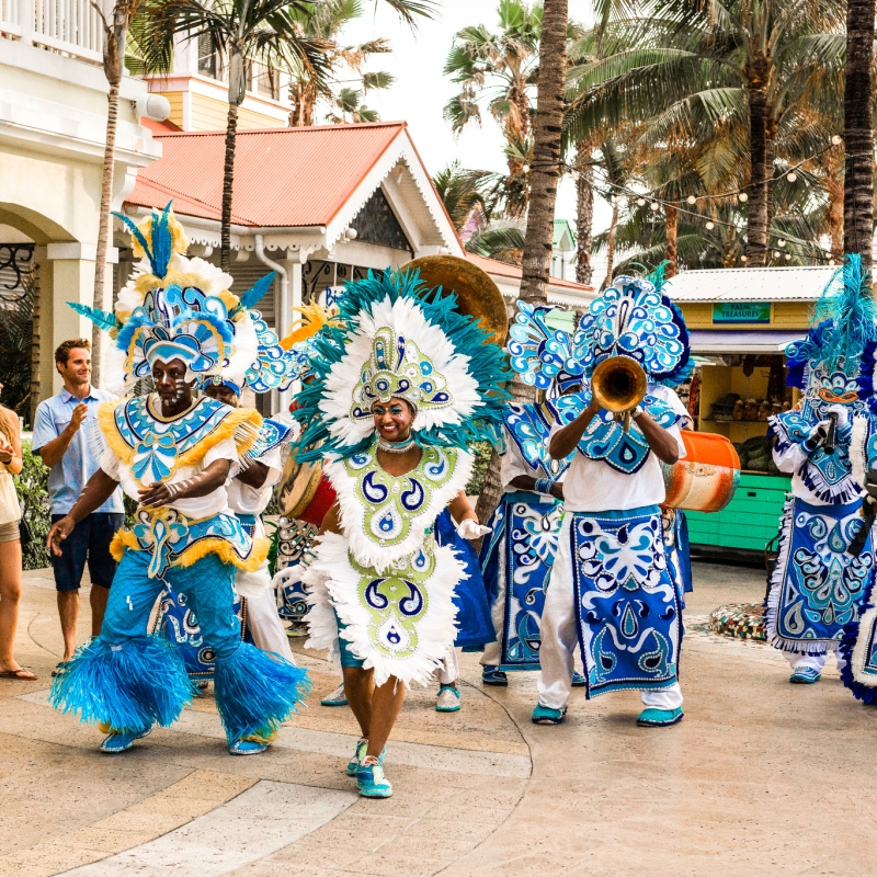 A Junkanoo band in colorful blue costumes plays instruments and dances outdoors in Nassau. 